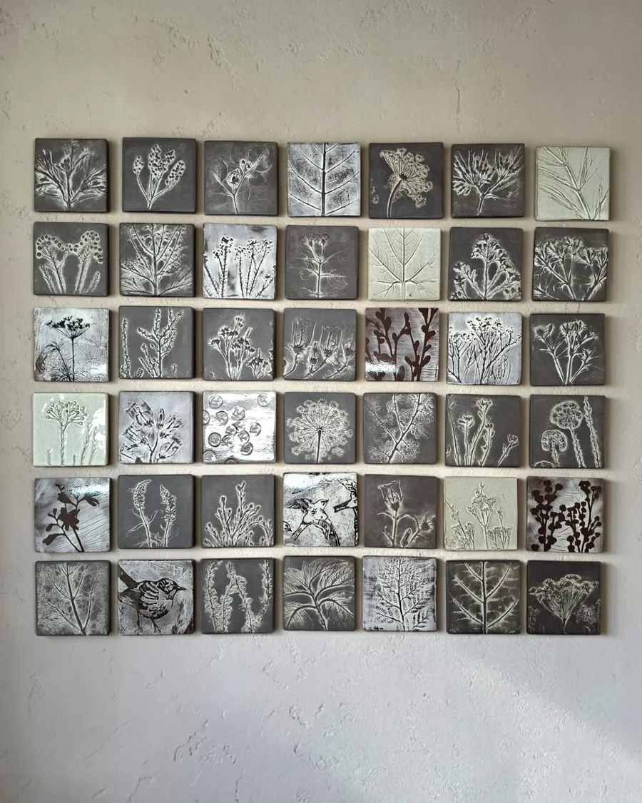 Wall installation of about forty small square tiles, each with a different plant impression